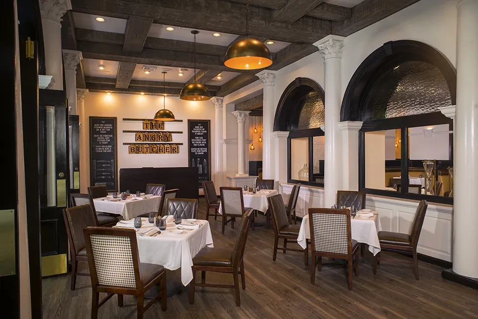 Restaurant dining room with dark beams, white walls, and "THE ANGRY BUTCHER" sign.