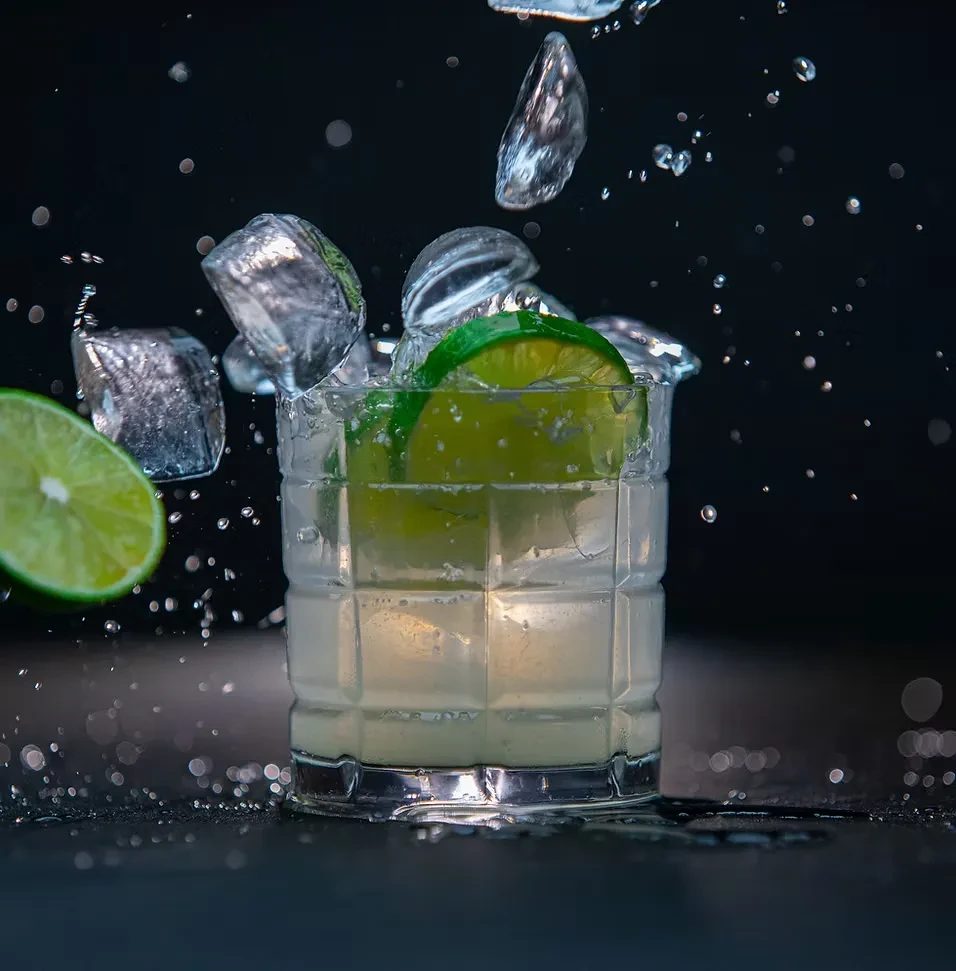 Refreshing drink with lime wedge, ice splashing against a dark background.