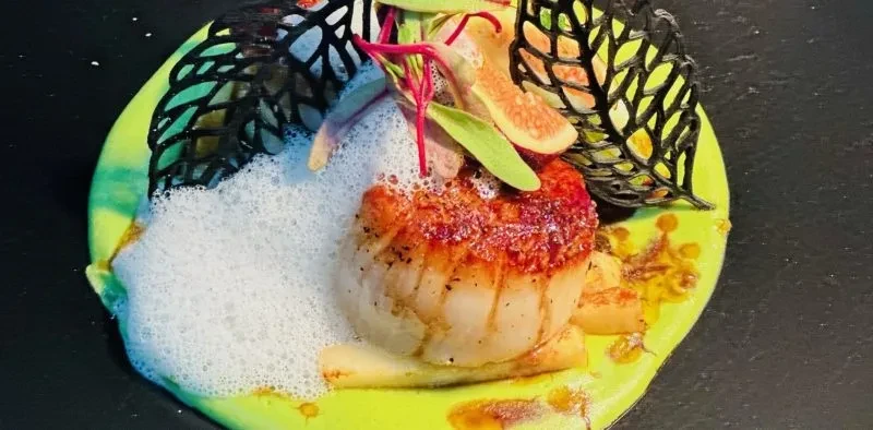 Seared scallop on green puree with white foam and fig garnish.