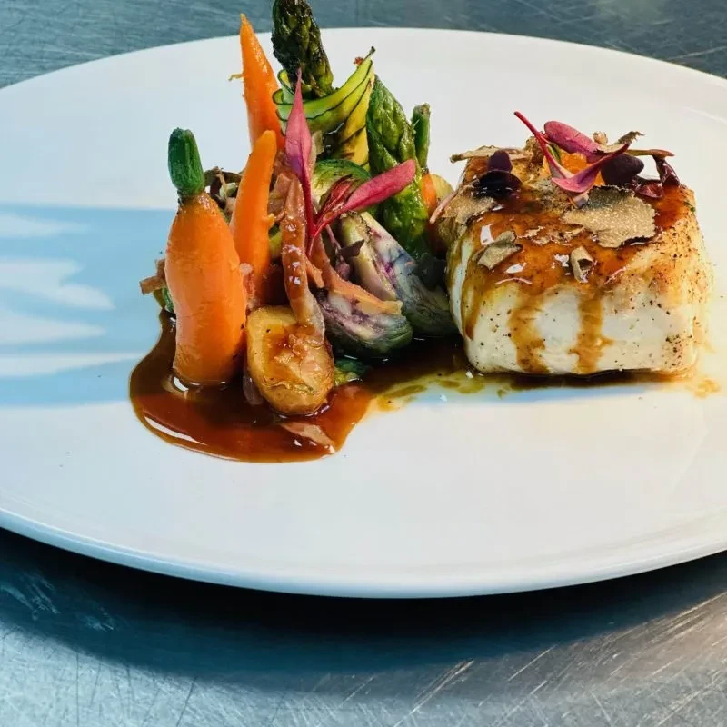 Gourmet dish: white fish, colorful vegetables, dark sauce, and truffle.