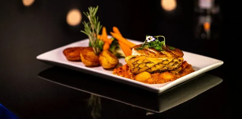 Plated crispy fish, chunky sauce, roasted potatoes, and vegetables.