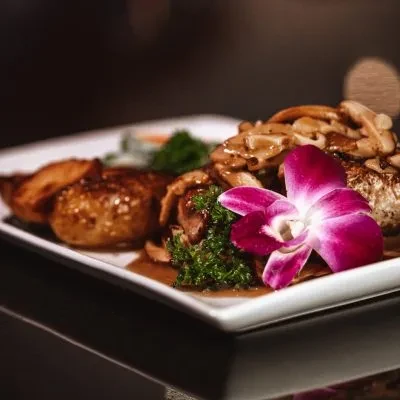 Plated gourmet meal with mushrooms, potatoes, parsley, and an orchid.