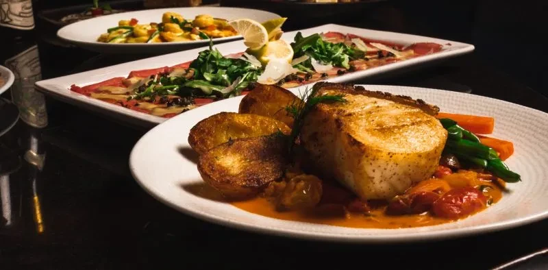Multiple gourmet dishes including seared fish, carpaccio, and pasta.