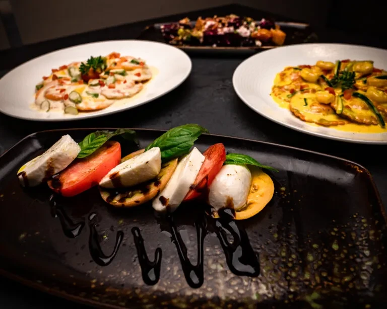 Overhead view of four distinct dishes, including Caprese, on a dark table.