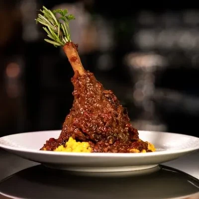 Braised lamb shank with dark red sauce, rosemary, and yellow polenta.