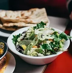 White bowl of green salad and flatbread on a red table.