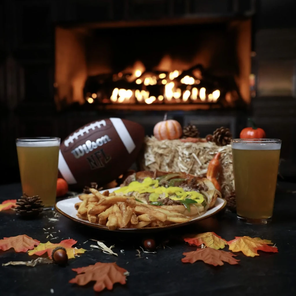 Sub sandwich, fries, beer, and football in an autumnal fireplace scene.