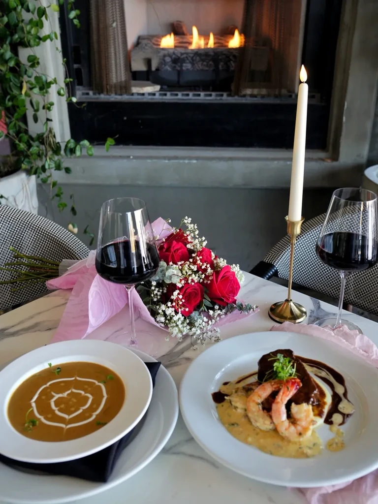 Dining table for two with gourmet food, roses, wine, fireplace.