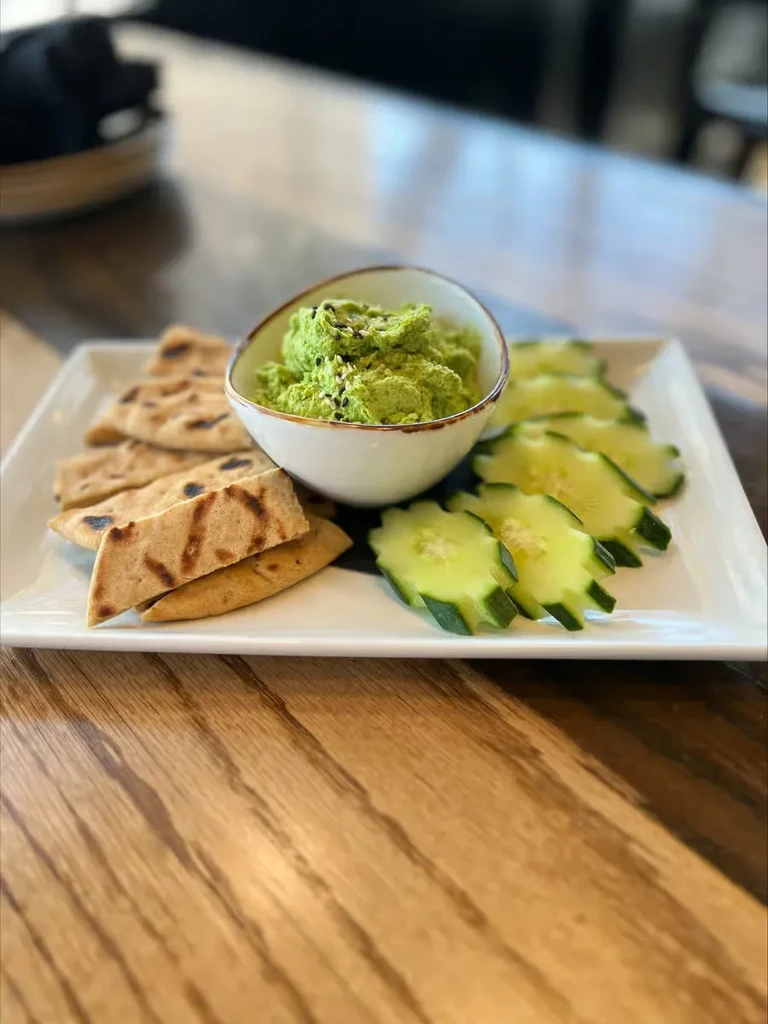 White plate with guacamole, flatbread triangles, and crinkle-cut cucumbers.