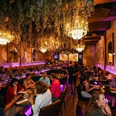 Restaurant interior: lush foliage, crystal chandeliers, brick walls, purple uplighting, diners.