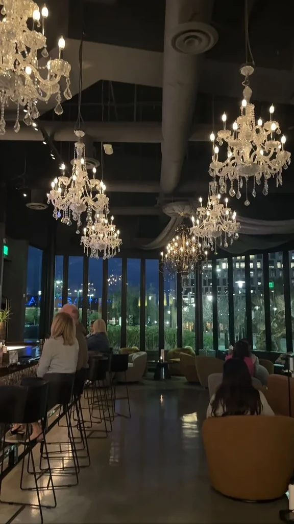 Dimly lit restaurant interior with prominent crystal chandeliers and city night view.