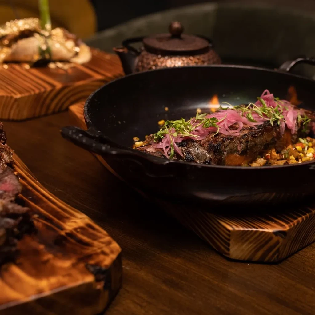 Seared meat with onions and microgreens in a cast-iron pan.