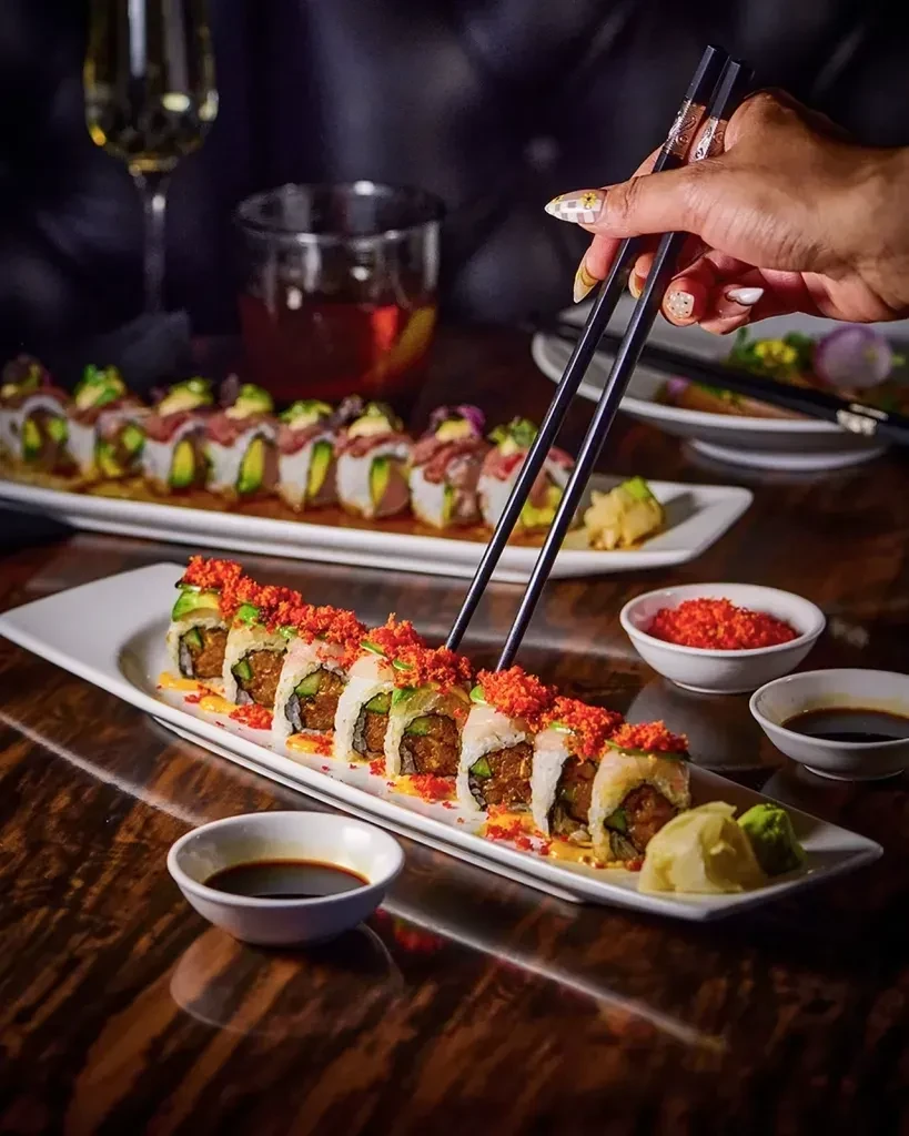 Platter of garnished sushi rolls, chopsticks, sauces, and drinks.