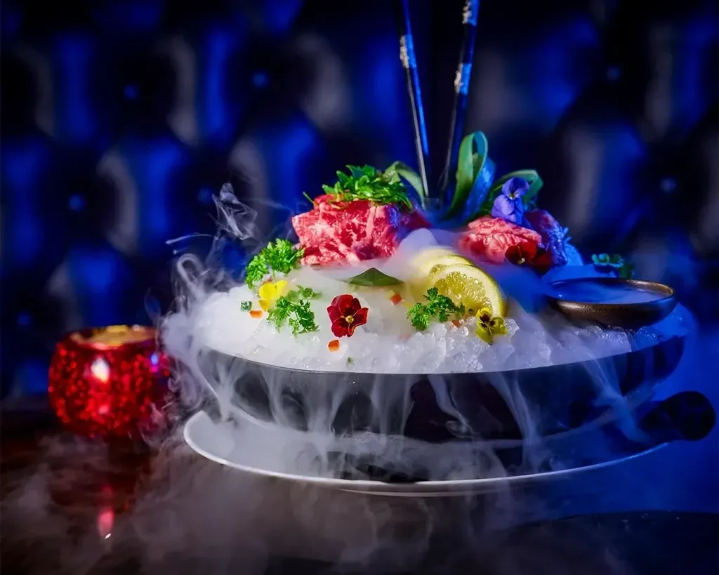 Theatrical raw meat dish with chopsticks, crushed ice, and dry ice smoke.