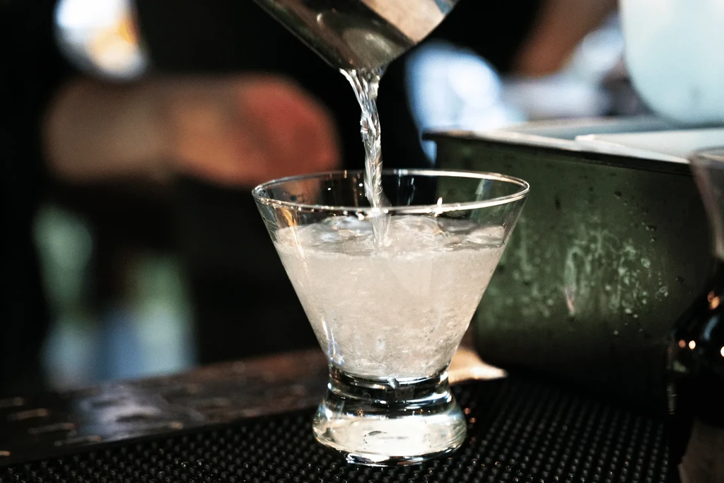 Clear liquid pours into an iced stemmed glass, creating a splash.