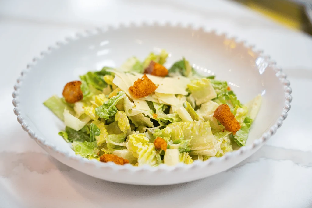 Caesar salad in white bowl with romaine, Parmesan, and golden croutons.