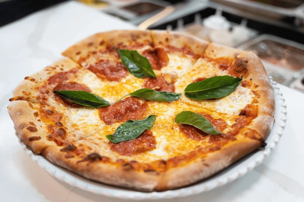 Freshly baked, sliced pepperoni pizza with mozzarella and basil on a plate.