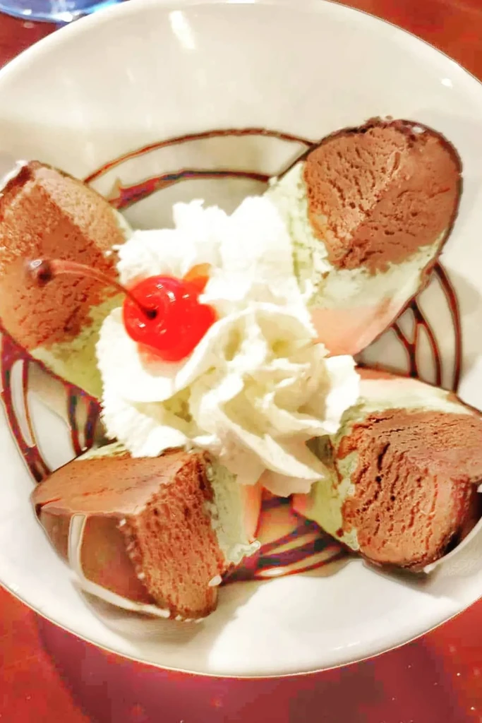 Layered chocolate, green, and pink dessert with whipped cream and cherry.