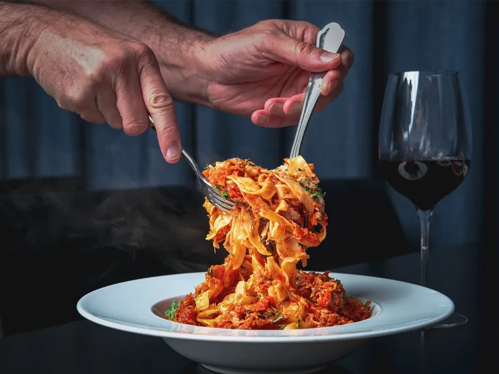 Hands actively twirling steaming red sauce pasta with forks.