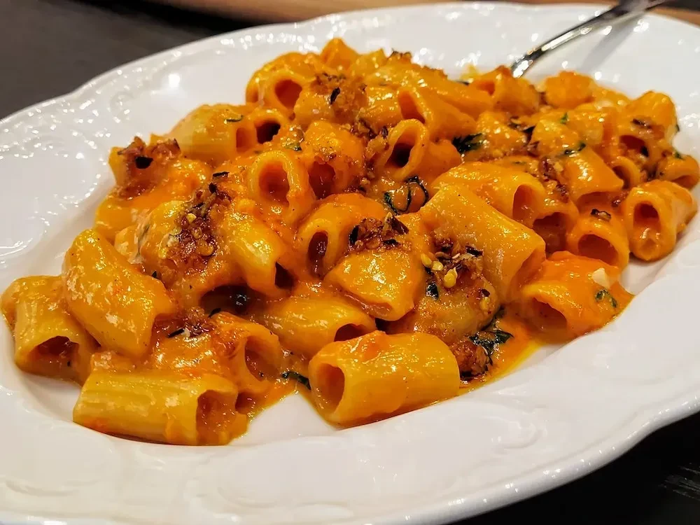 Close-up of creamy red-orange tubular pasta with herbs and a fork.