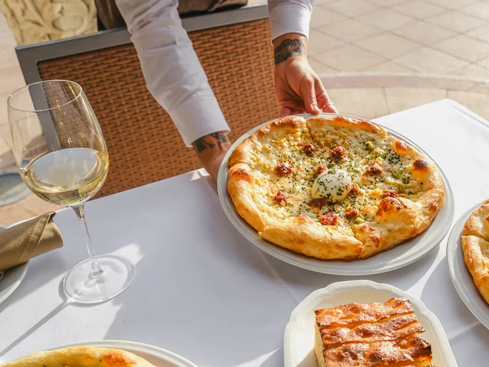 Tattooed hand placing cheesy flatbread with herbs and creamy center.