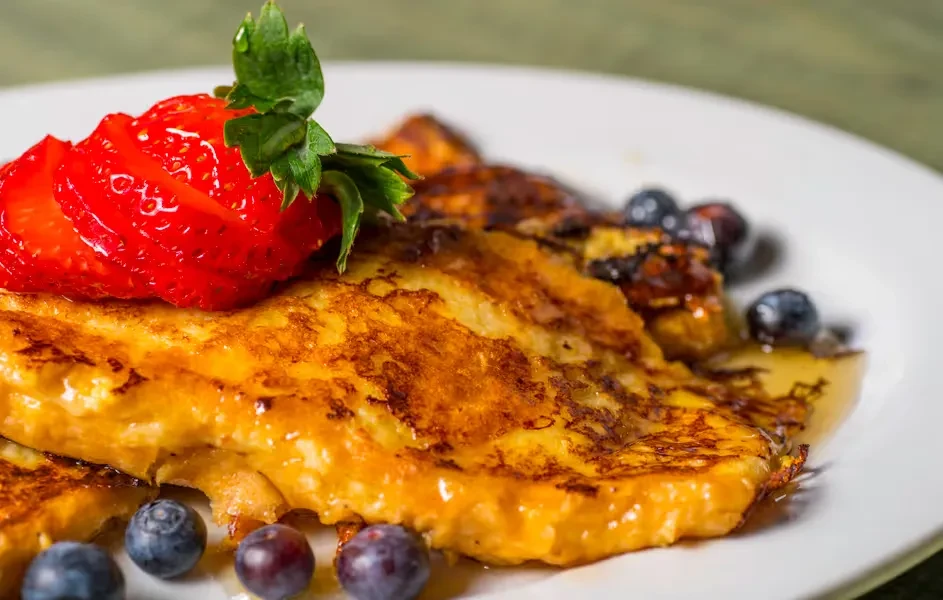 Golden French toast stack with strawberries, blueberries, and syrup.