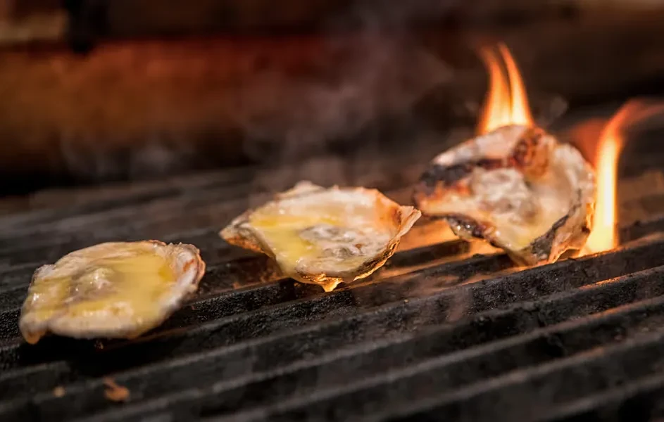 Three oysters grilling with melting butter and active flames.