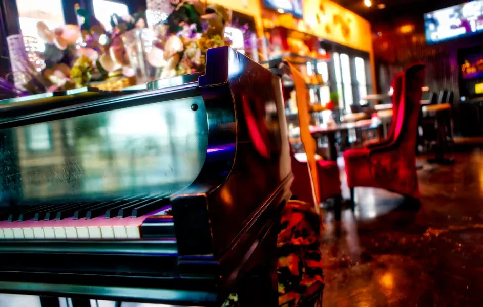 Dark, reflective piano in a vibrant, out-of-focus bar interior.