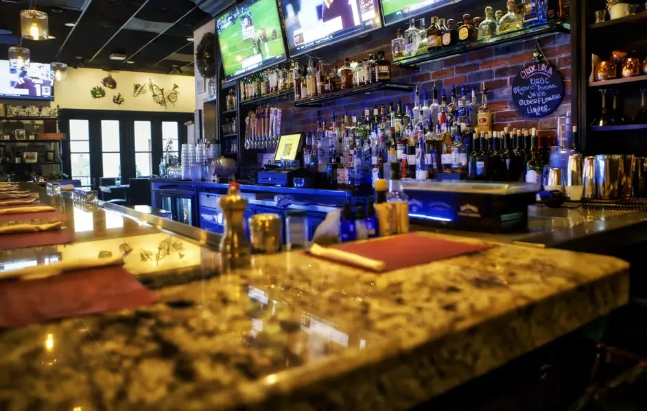 Modern sports bar interior with stocked bar, granite counter, and sports TVs.