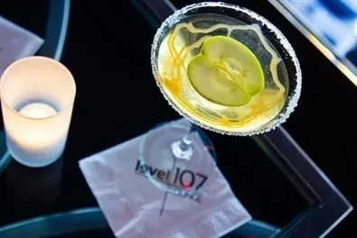 Green apple cocktail with caramel swirls, candle, and 'level 107 lounge' napkin.