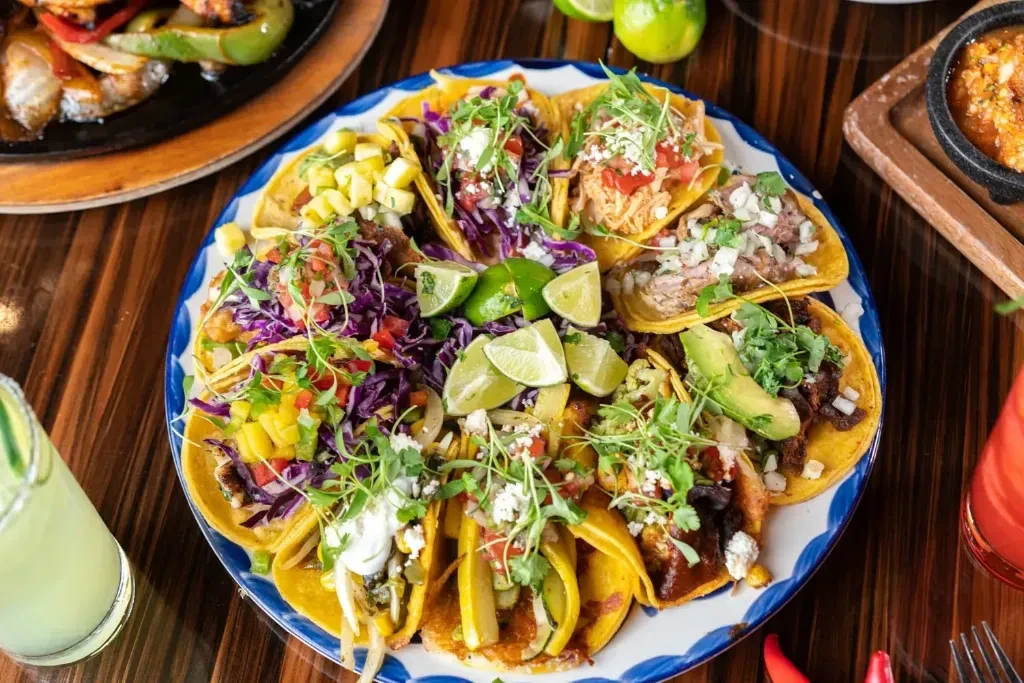 Platter of numerous tacos with diverse fillings and lime wedges.
