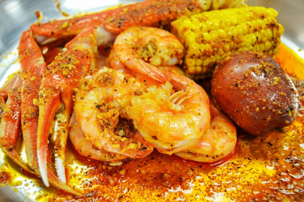 Reddish-orange seafood boil with crab legs, shrimp, corn, and potato.