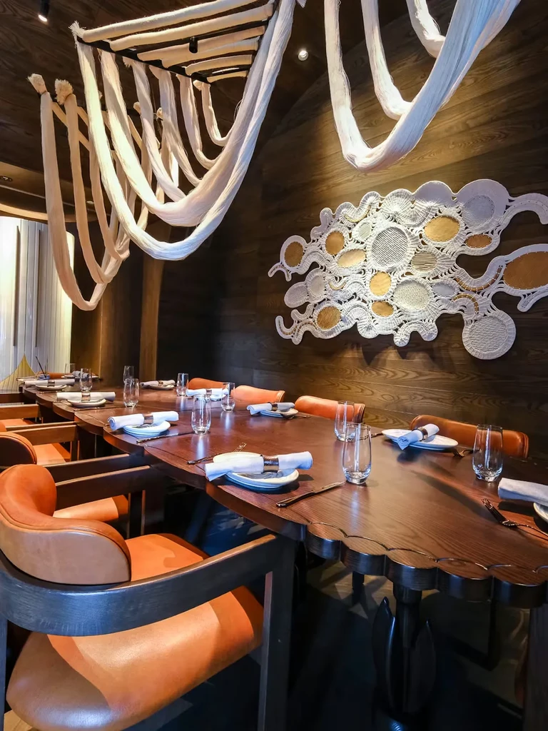 Warm restaurant interior with dark wood wave-edged table and cloud ceiling.