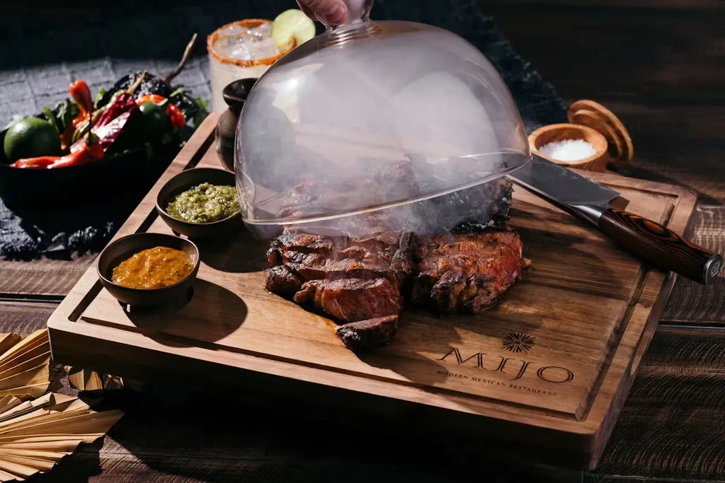 Hand lifting cloche from smoking meat at Mijo Modern Mexican.