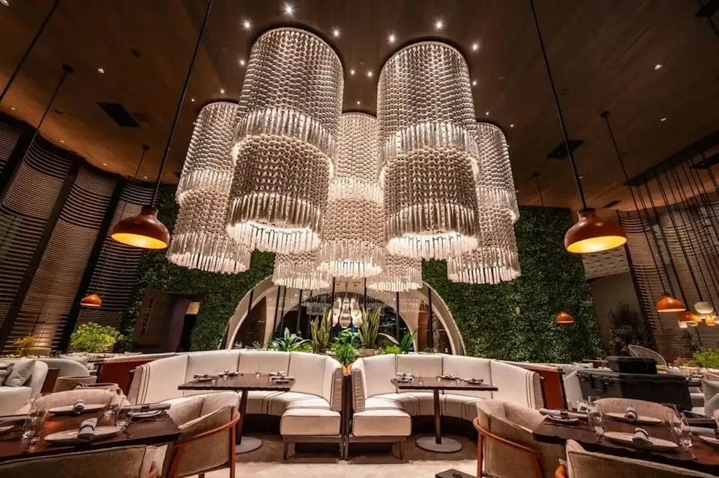 Luxurious modern restaurant interior with cylindrical chandeliers, wood panels, and a green wall.
