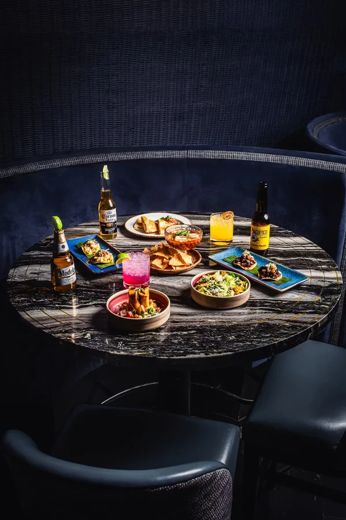 Mexican food spread with beers and cocktails on a dark marble table.