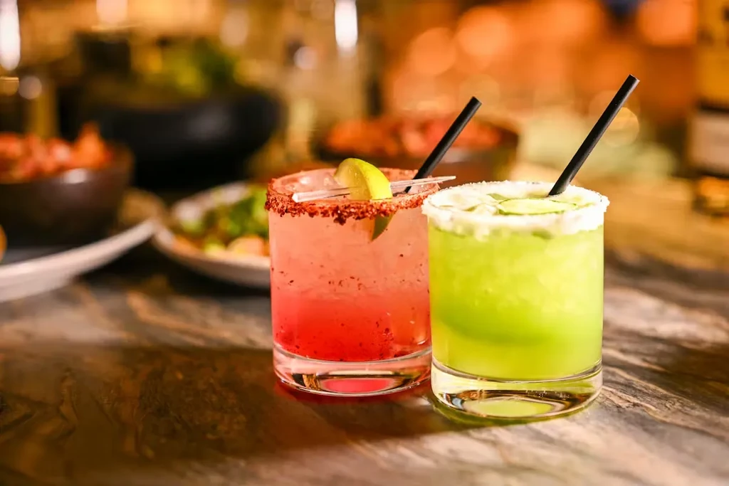 Two vibrant cocktails, red-pink with dark rim and green with cucumber.