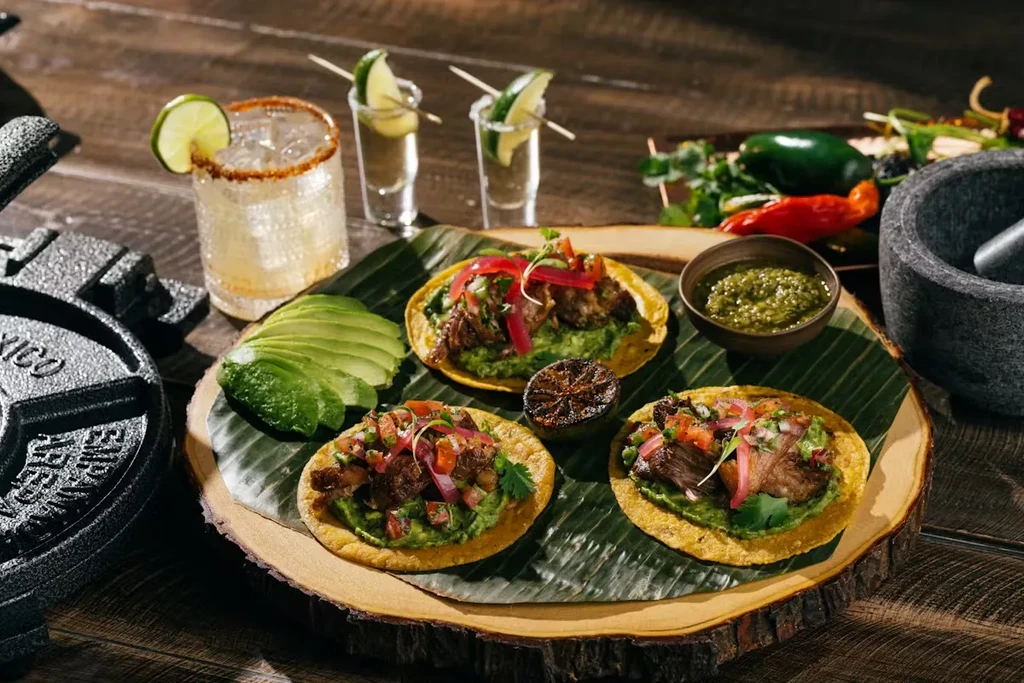 Vibrant Mexican tacos, salsa, avocado, margarita, and tequila shots on wood.