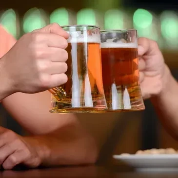 Two people clink glass mugs of golden and dark beer.