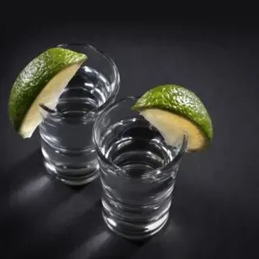 Two clear shot glasses with liquid and lime wedges on dark background.