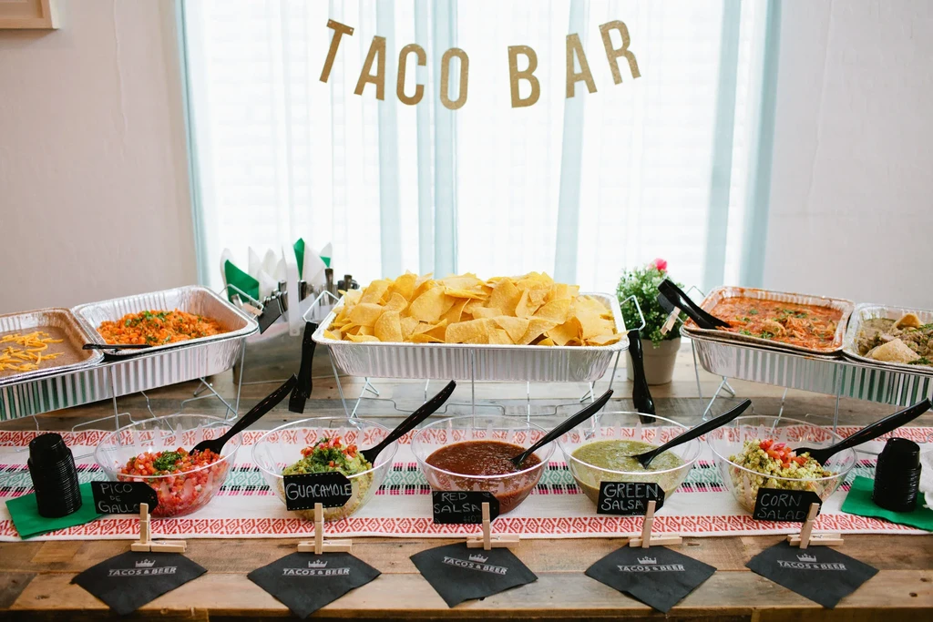A festive taco bar setup with various hot dishes and fresh toppings.