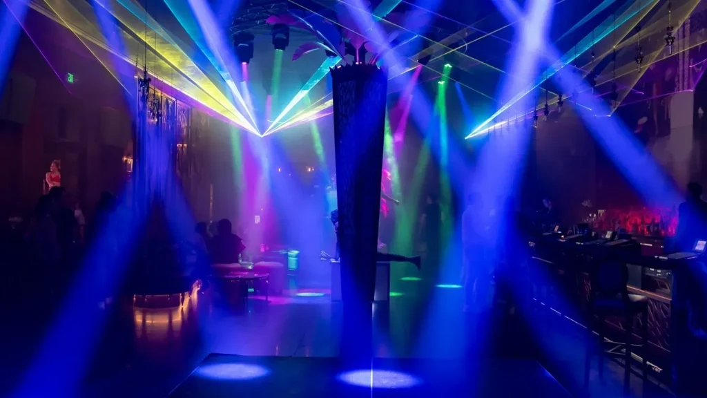 Hazy club interior with vibrant laser show, performer, and people.