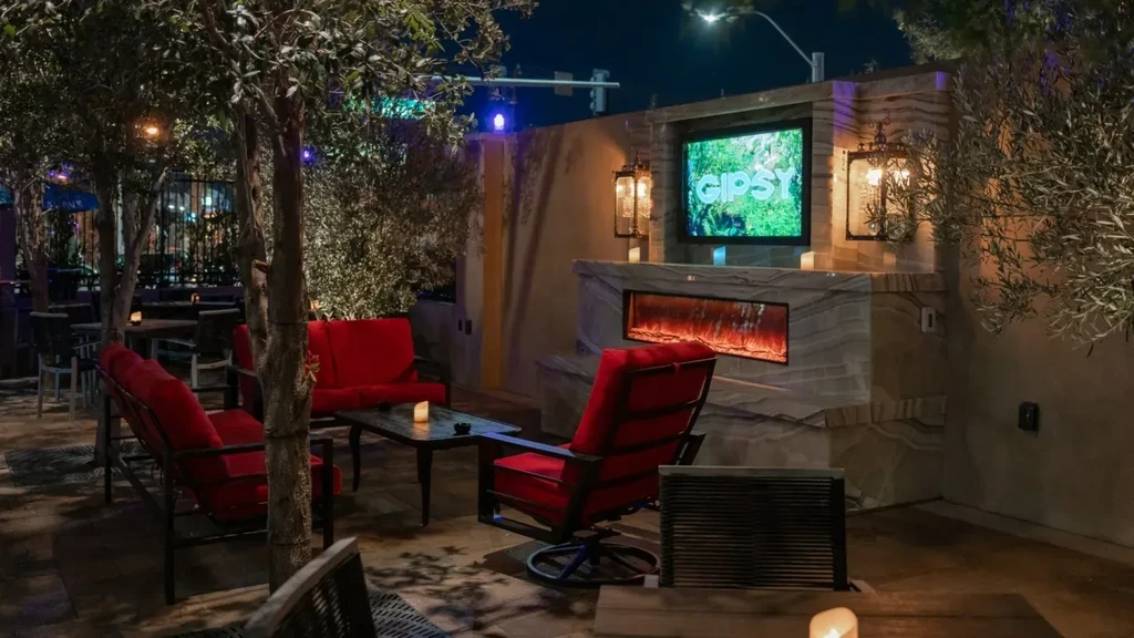Outdoor patio at night with red seating, fireplace, and GIPSY logo.