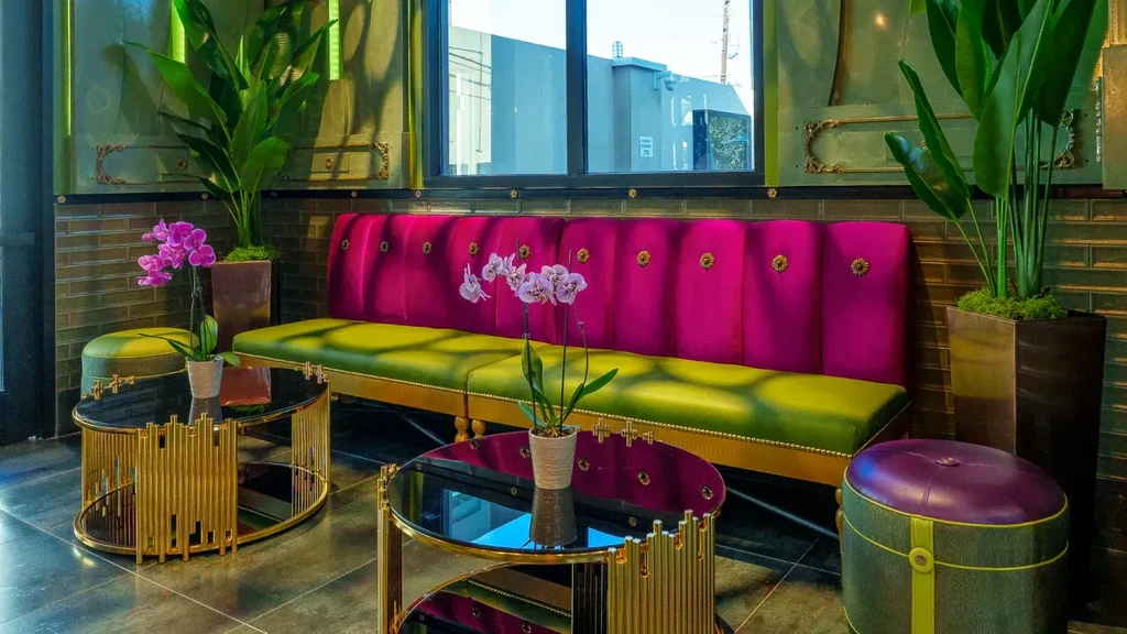 Vibrant lounge with fuchsia-lime sofa, gold tables, and purple orchid.