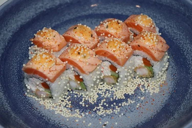 Eight sushi rolls topped with seared salmon, sauce, and garnish.