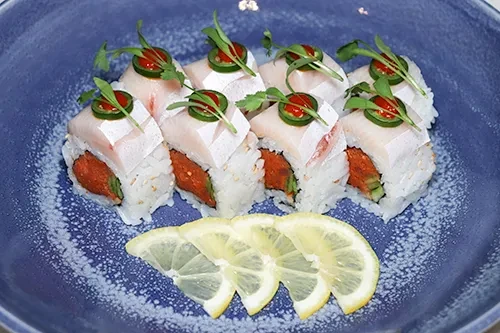 Eight sushi rolls on a blue plate with fish, jalapeño, and lemon.