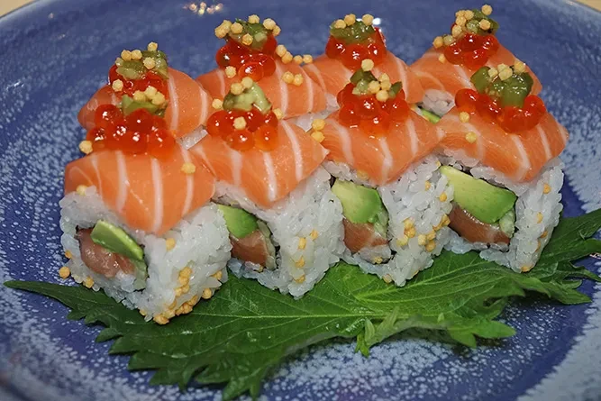 Eight salmon avocado sushi rolls with roe on a ceramic plate.