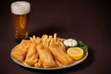 Golden fish and chips with tartar sauce, lemon, and beer.