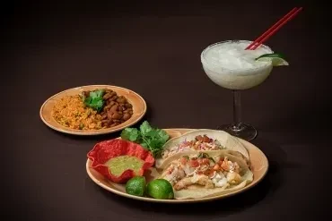 Two plates of Mexican tacos, rice, beans, chips, and a margarita.
