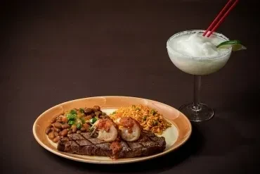 Plated grilled meat meal with rice, pinto beans, and a margarita.